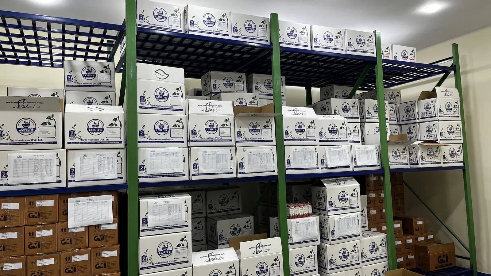 Finished-goods warehouse with rows of white LORD’S shipper cartons on blue and green steel racking